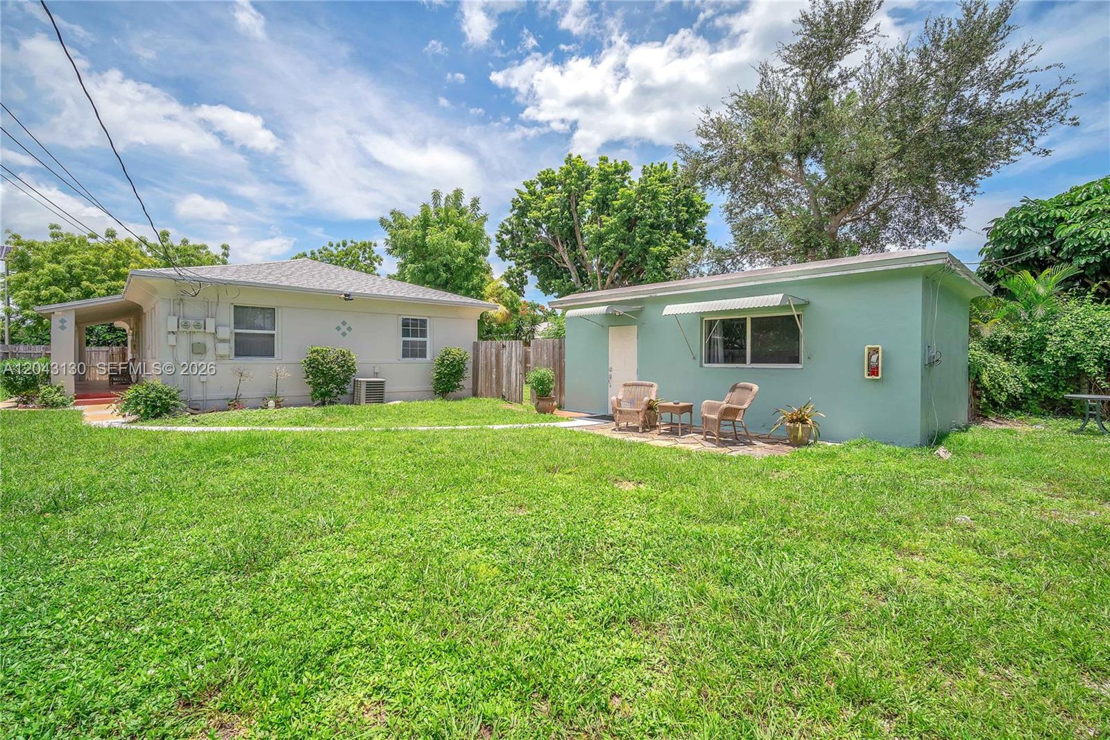 A grassy backyard features a light-colored main house and a detached teal-colored structure — 261 SW 15th St # 1, Dania Beach FL 33004, DANIA BEACH, FL