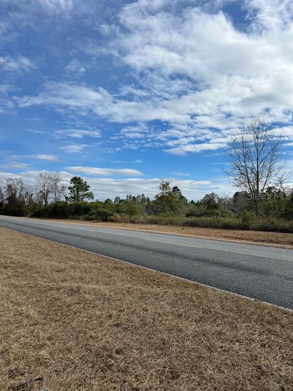 A paved road runs alongside a grassy field with trees under a cloudy blue sky — 00 SW CR 249, JASPER, FL