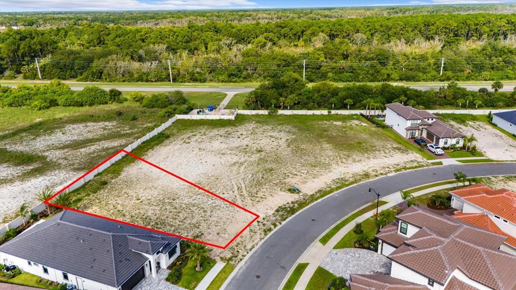 An aerial view shows a vacant residential lot outlined in red next to suburban homes — 74 DEL PALMA DRIVE, PALM COAST, FL
