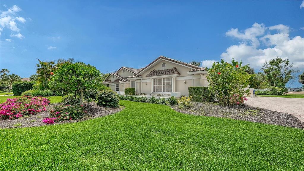 A single-story house with a beige exterior, tiled roof, and landscaped lawn under a blue sky — 3988 LOSILLIAS DRIVE, SARASOTA, FL