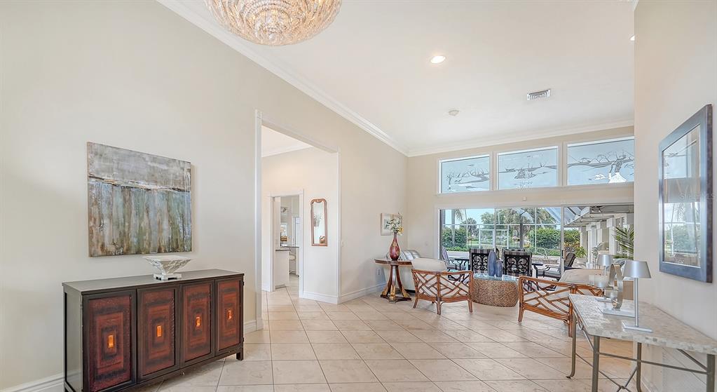 A bright living room features tile floors, a crystal chandelier, and large windows overlooking a patio — 3988 LOSILLIAS DRIVE, SARASOTA, FL