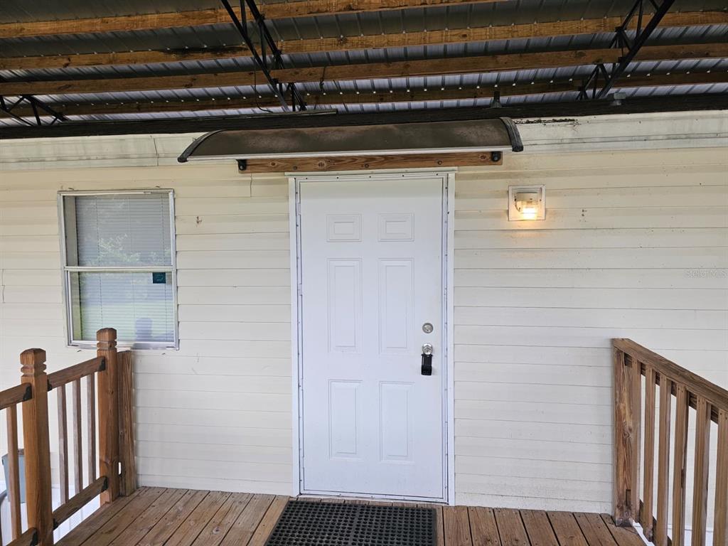A white exterior door with a small awning is centered on a wooden porch — 9050 SE 196TH TERRACE, OCKLAWAHA, FL