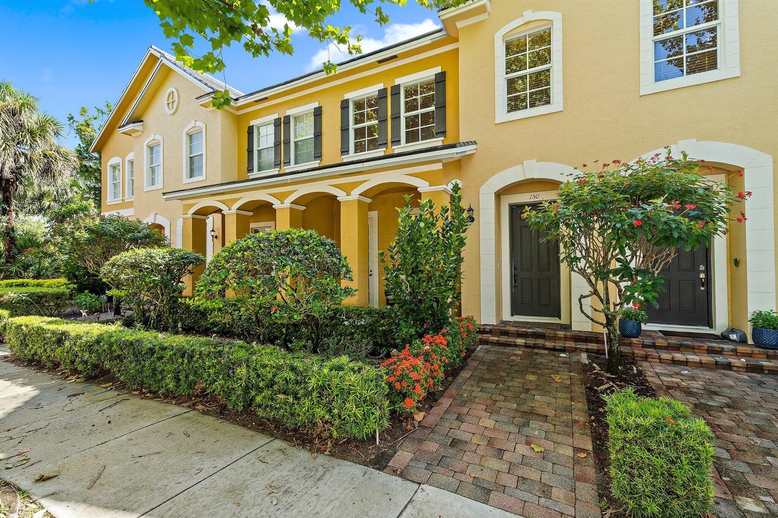 A yellow two-story townhouse exterior features arched entryways, dark doors, and a brick walkway — 150 Lismore Lane, Jupiter FL 33458, JUPITER, FL