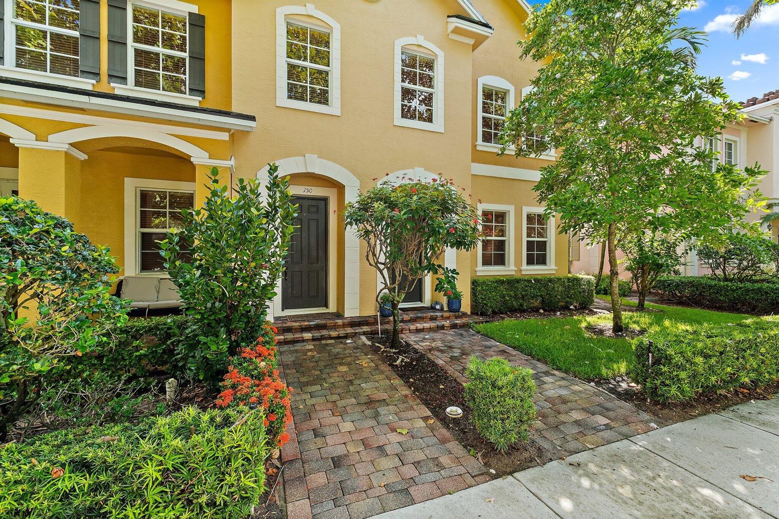 A yellow two-story townhouse features a brick walkway leading to a dark front door — 150 Lismore Lane, Jupiter FL 33458, JUPITER, FL
