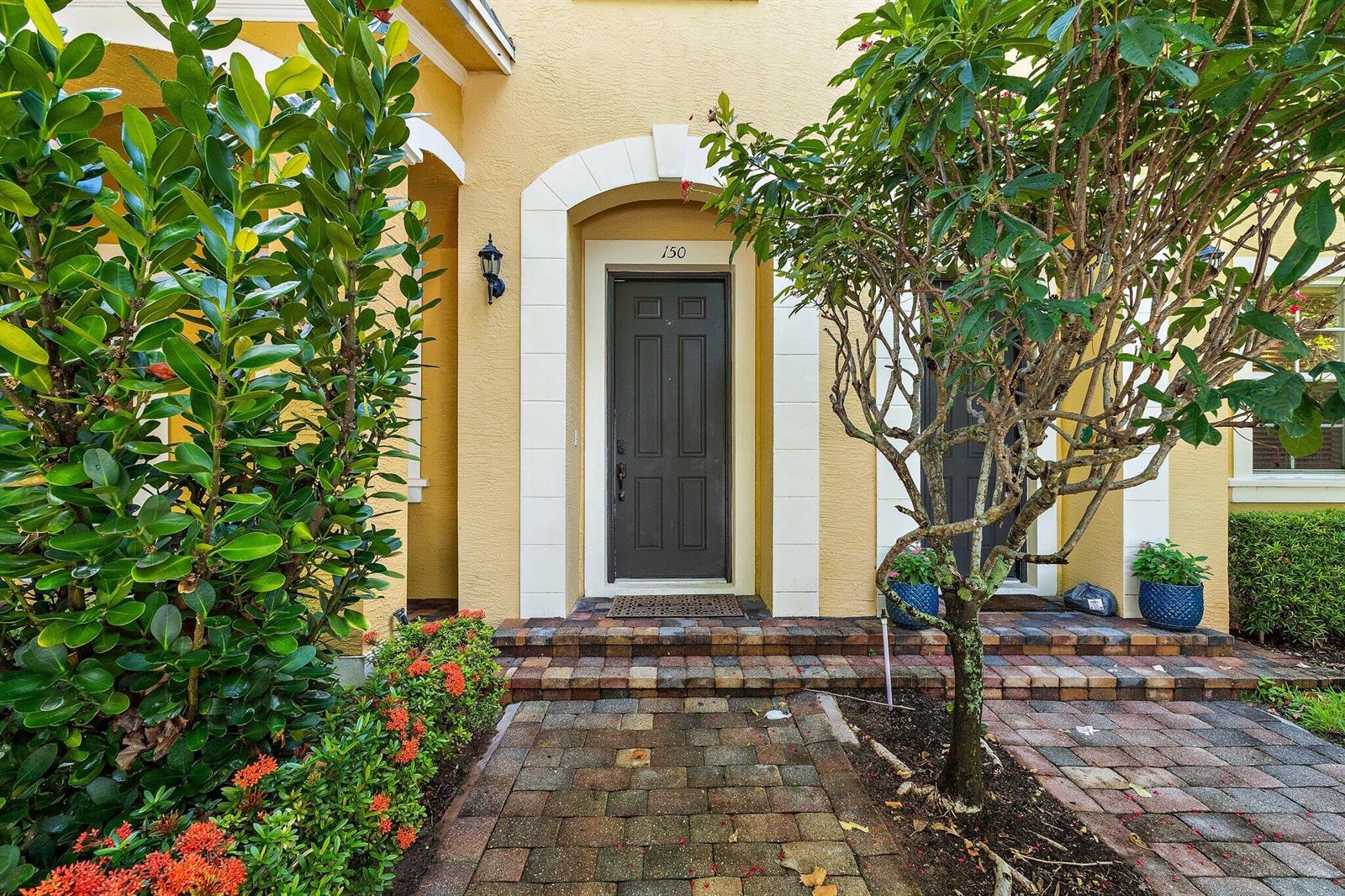 A front entrance with a dark door, brick steps, and landscaping against a yellow wall — 150 Lismore Lane, Jupiter FL 33458, JUPITER, FL