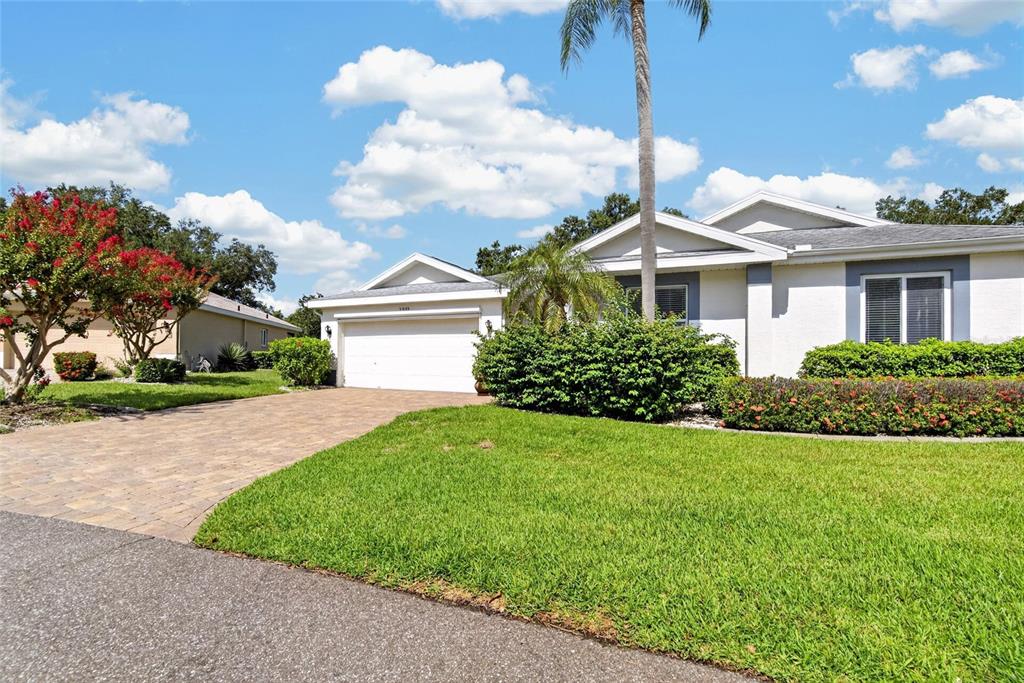 A single-story house with a white garage, paved driveway, and green lawn under a blue sky — 2222 MAYFIELD PALMS LANE UNIT 322, SUN CITY CENTER, FL