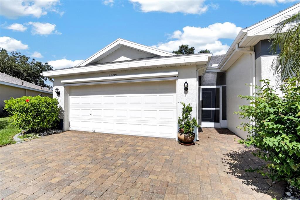 A paved driveway leads to a single-story home with a white garage and screened entryway — 2222 MAYFIELD PALMS LANE UNIT 322, SUN CITY CENTER, FL