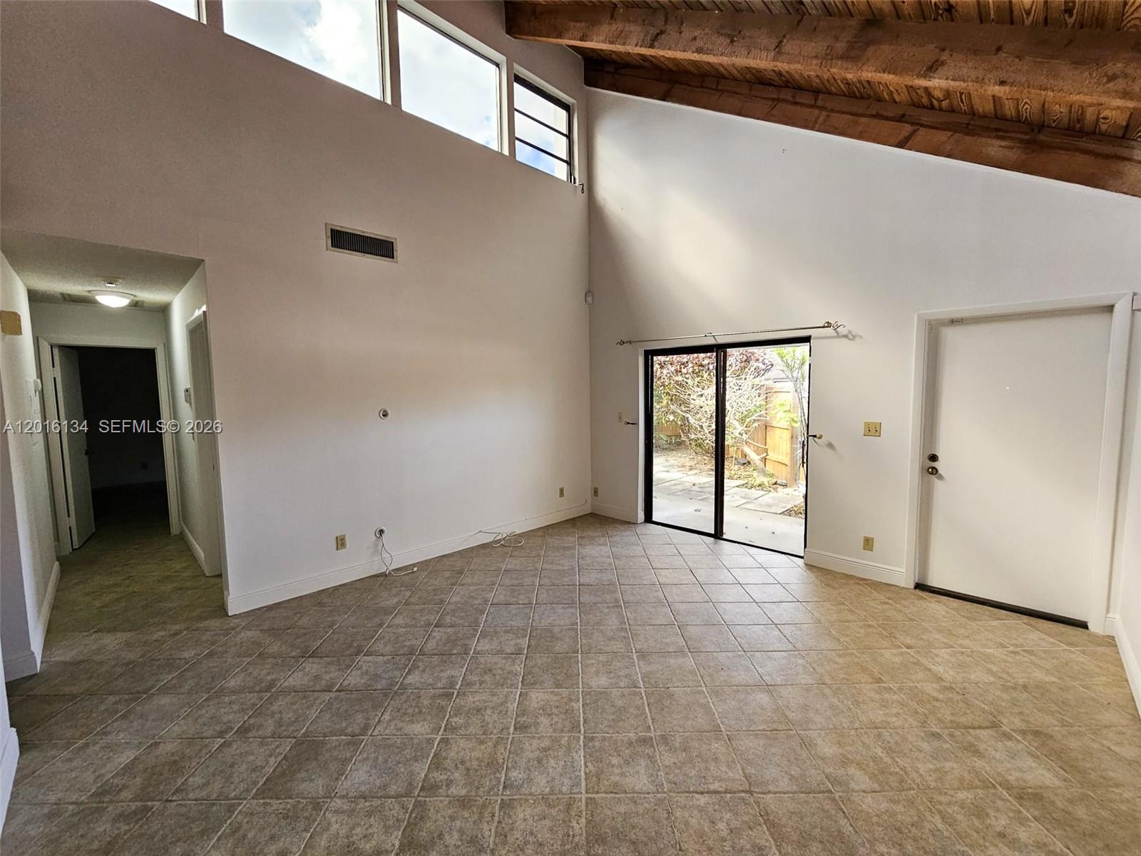 A living room features vaulted wood-beamed ceilings, tile flooring, and a sliding glass door — 7749 SW 100th St # 33, Miami FL 33156, MIAMI, FL