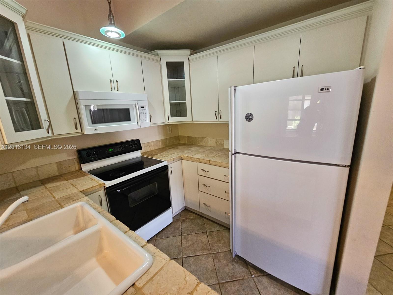 A kitchen features white cabinets, a white refrigerator, a black stove, and tiled countertops — 7749 SW 100th St # 33, Miami FL 33156, MIAMI, FL