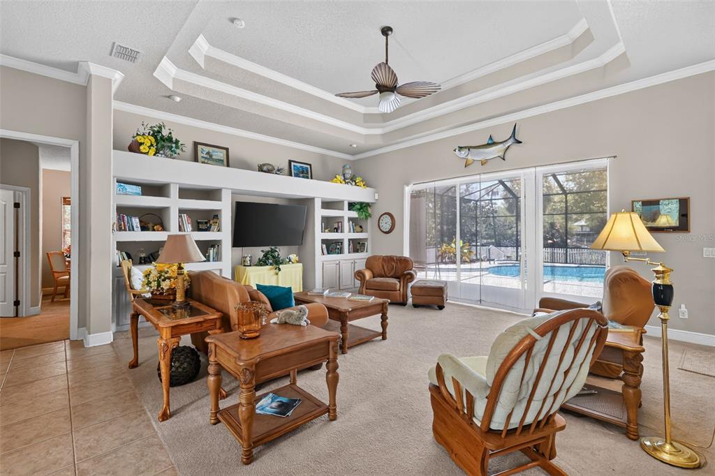 A living room features a tray ceiling, built-in shelving, a television, and sliding glass doors — 720 NORTHWEST SNUG HARBOR ROAD, CRYSTAL RIVER, FL