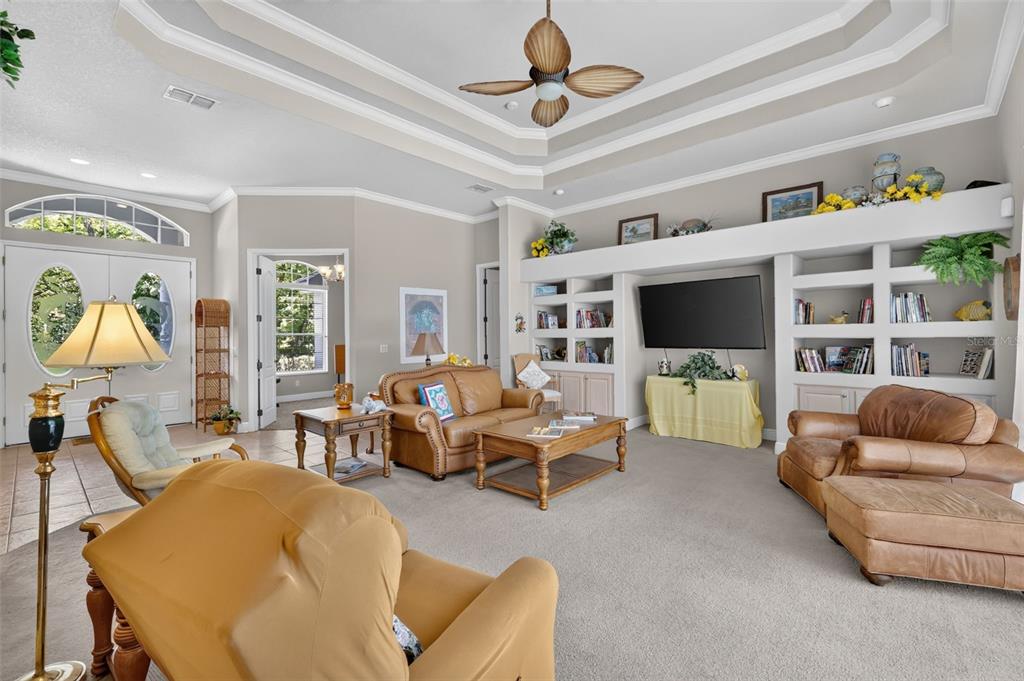 A living room features a tray ceiling, built-in shelving, a television, and tan leather furniture — 720 NORTHWEST SNUG HARBOR ROAD, CRYSTAL RIVER, FL