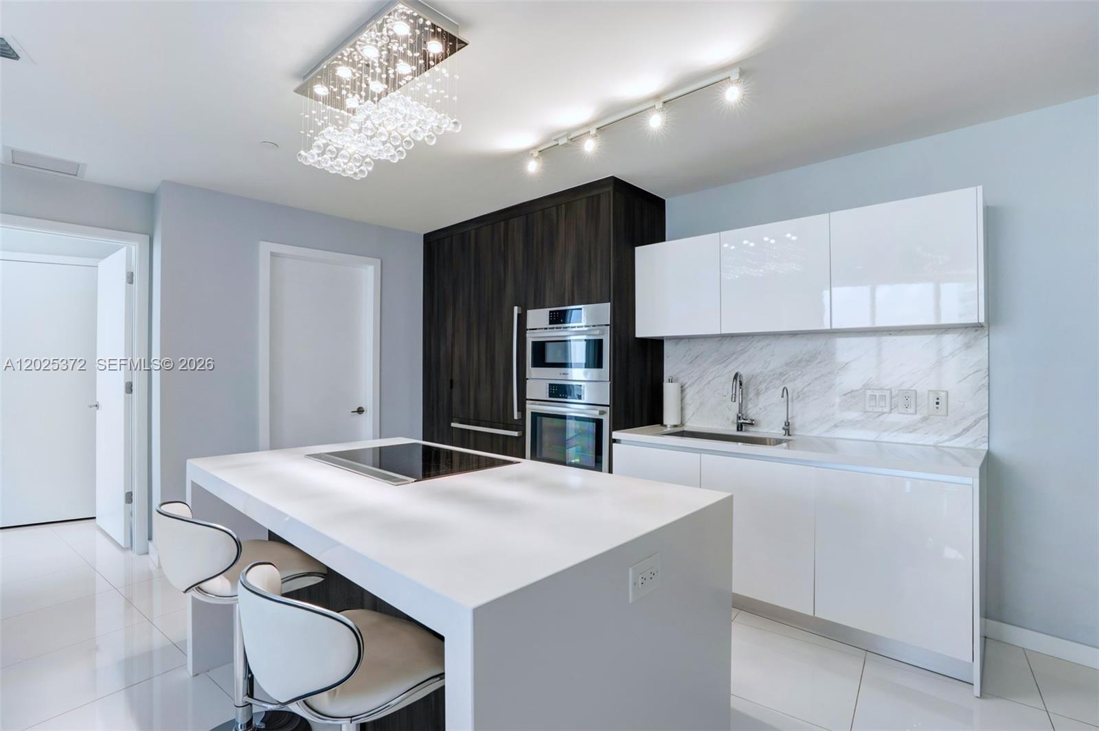 A modern kitchen features a white island with a cooktop, dark cabinetry, and white cabinets — 851 NE 1st Ave # 3909, Miami FL 33132, MIAMI, FL