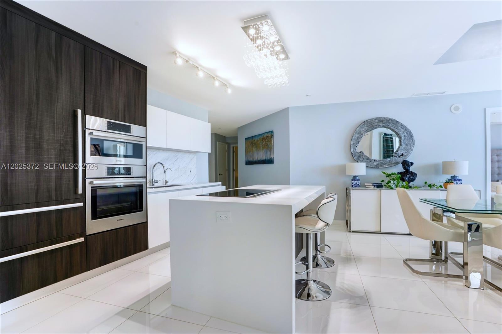 A modern kitchen features dark wood cabinetry, a white island, and a glass dining table — 851 NE 1st Ave # 3909, Miami FL 33132, MIAMI, FL