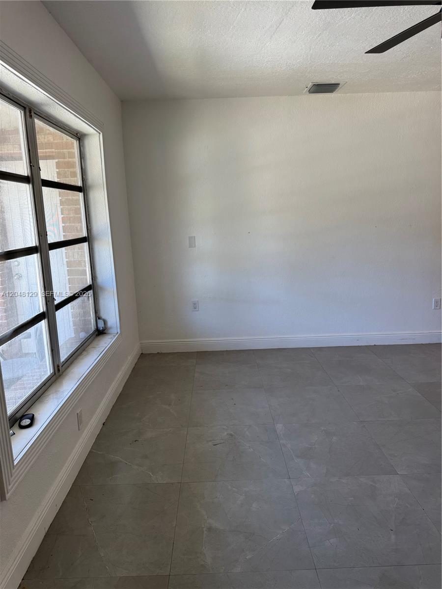 An empty room features gray tile flooring, white walls, and a large multi-pane window — 1281 NE 209th Ter, Miami FL 33179, MIAMI, FL