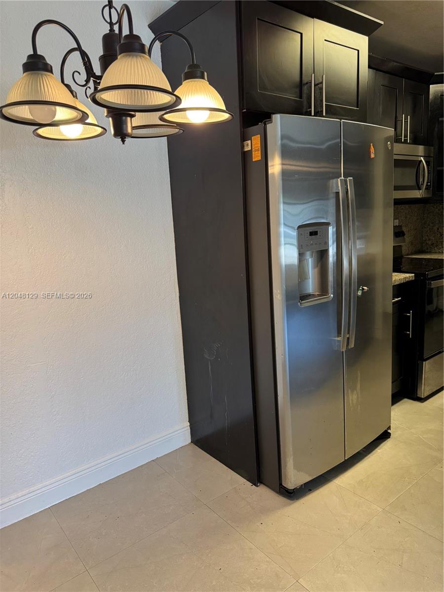 A stainless steel refrigerator is positioned next to dark cabinets in a kitchen area — 1281 NE 209th Ter, Miami FL 33179, MIAMI, FL