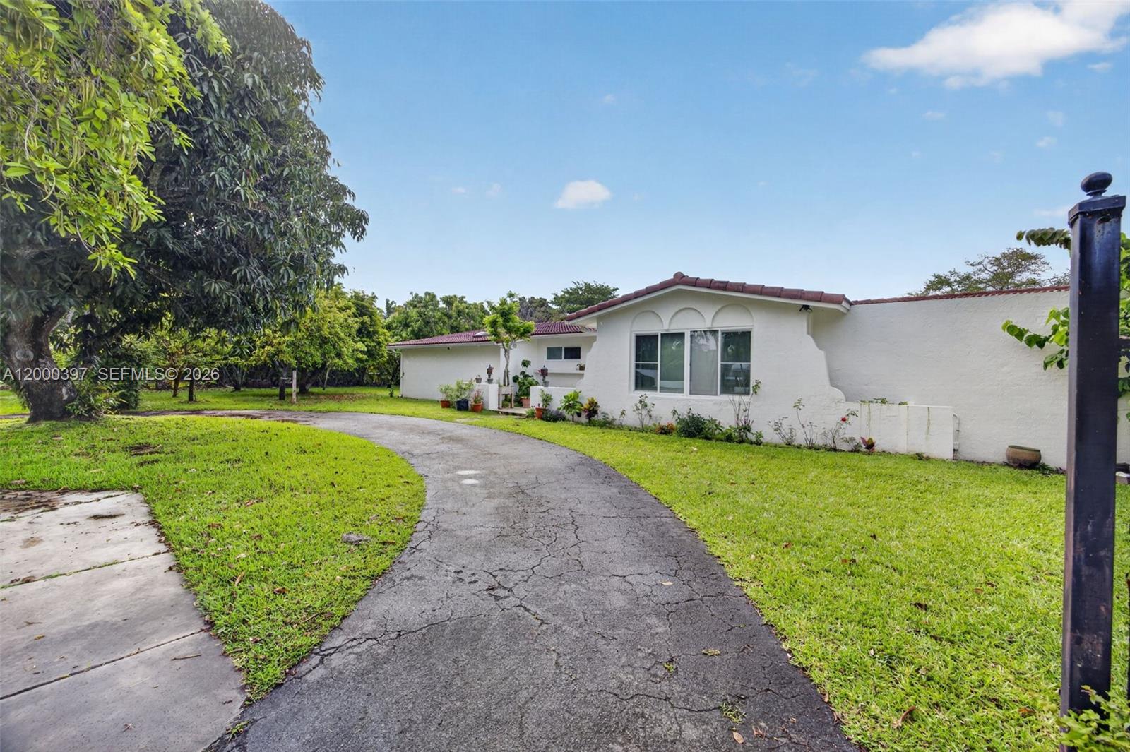 A white, single-story house with a curved driveway and a large tree in the yard — 7690 SW 128th St # 0, Pinecrest FL 33156, PINECREST, FL