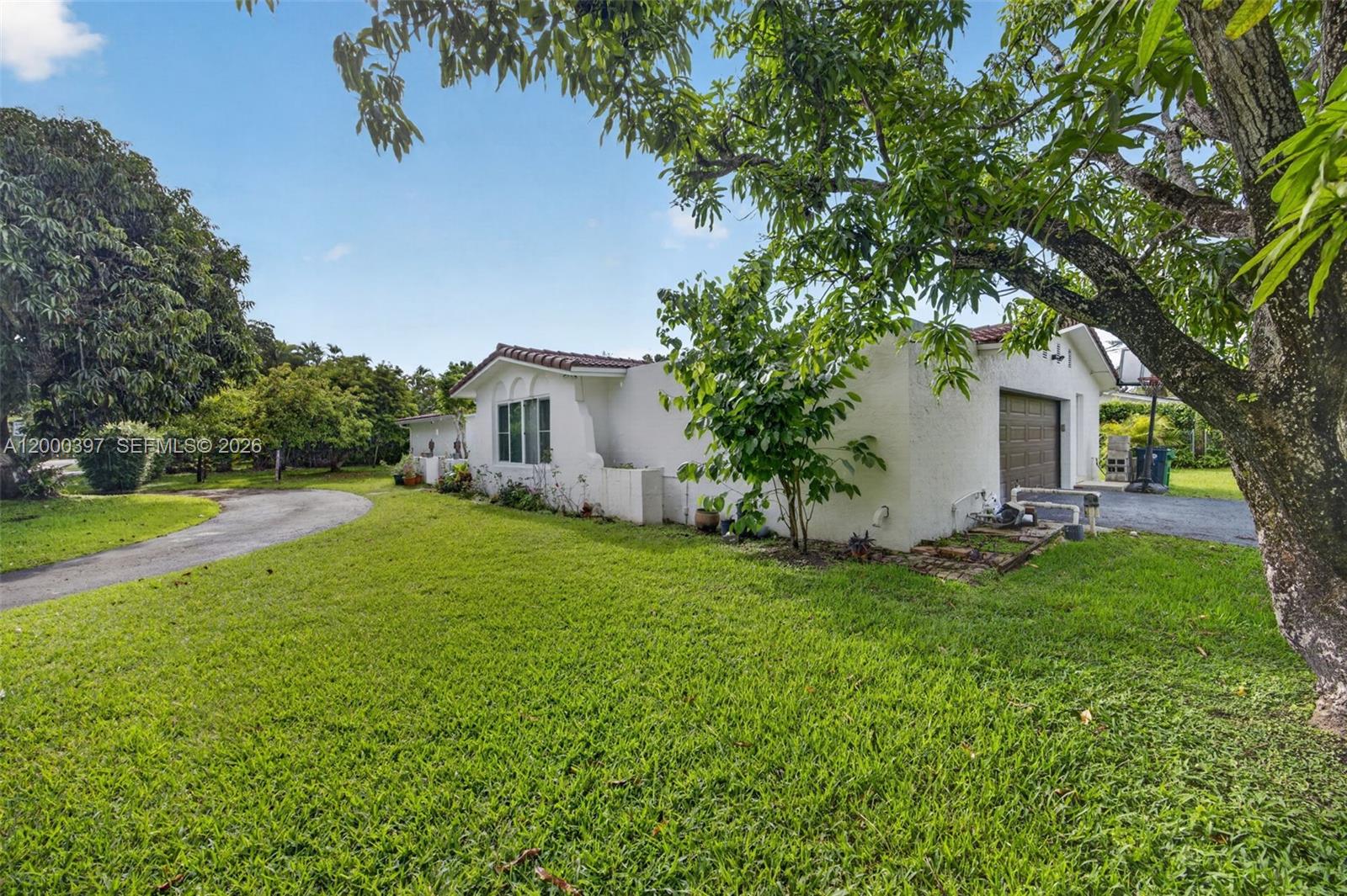 A white single-story house with a brown garage door sits on a grassy lot — 7690 SW 128th St # 0, Pinecrest FL 33156, PINECREST, FL