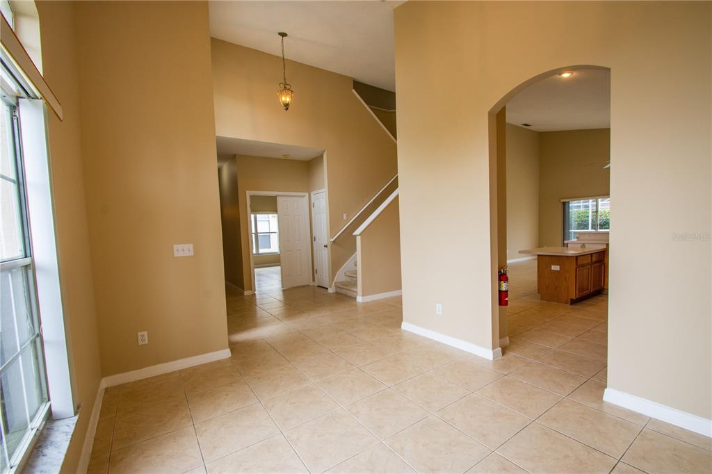 An interior view shows a tiled room with a staircase, arched entryway, and kitchen area — 421 LOCKBREEZE DRIVE, DAVENPORT, FL