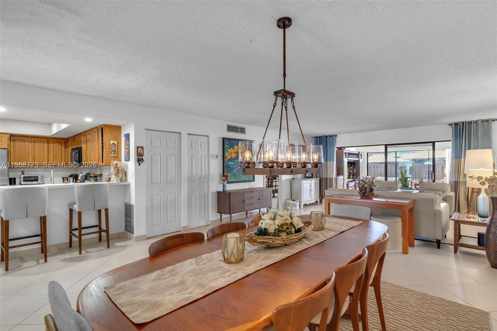 A dining area with a wooden table and chandelier opens into a kitchen and living room — 11378 SW 84th Ln, Miami FL 33173, MIAMI, FL