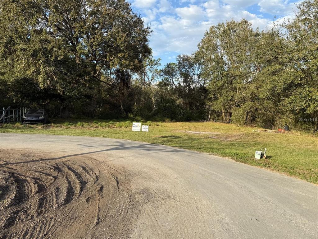 A vacant, grassy lot sits along a curved paved road near a wooded area — CANAL COURT, LAKE WALES, FL