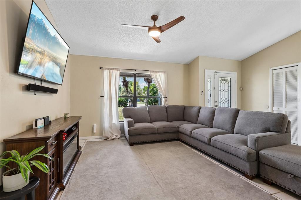 A living room features a grey sectional sofa, a wall-mounted television, and a ceiling fan — 6805 LONGPOINTE WAY, TAMPA, FL