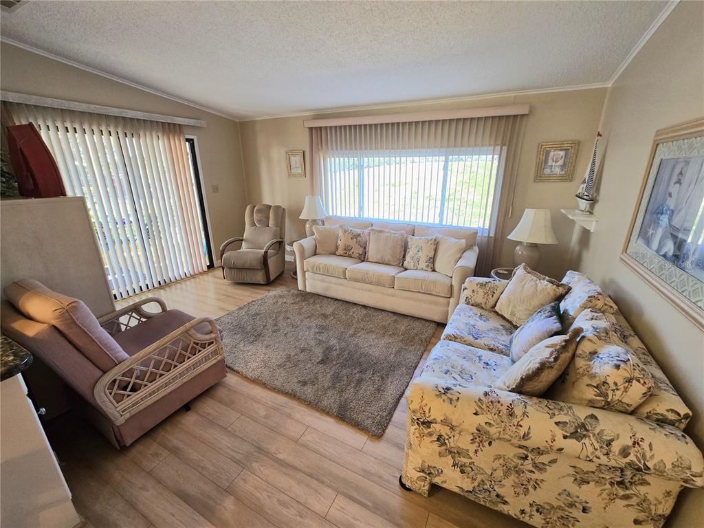 A living room features light wood flooring, a beige sofa, floral seating, and vertical blinds — 8503 PRINCESS COURT, PALMETTO, FL