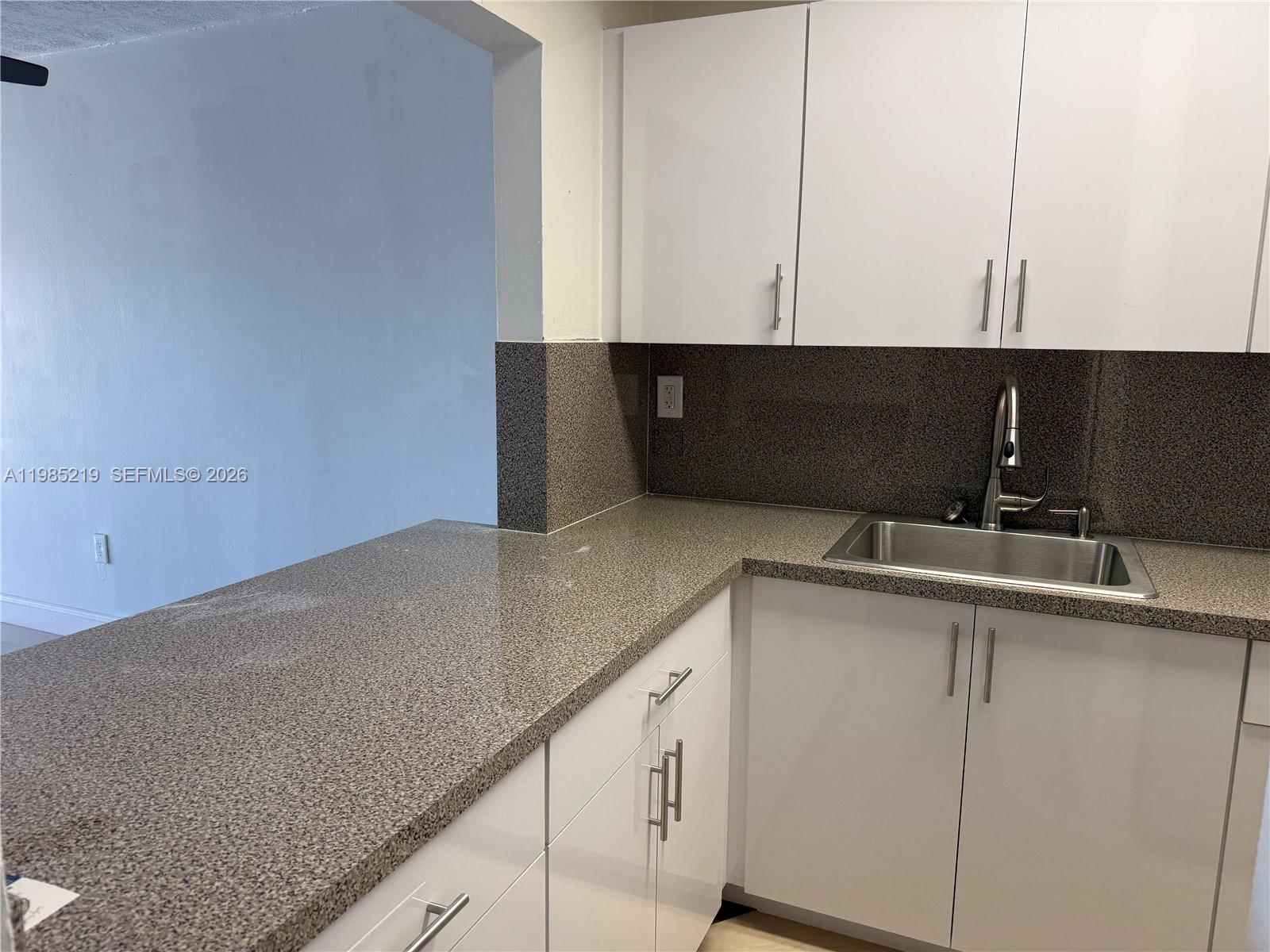 A kitchen features white cabinets, speckled countertops, and a stainless steel sink — 6055 W 19th Ave # 311, Hialeah FL 33012, HIALEAH, FL