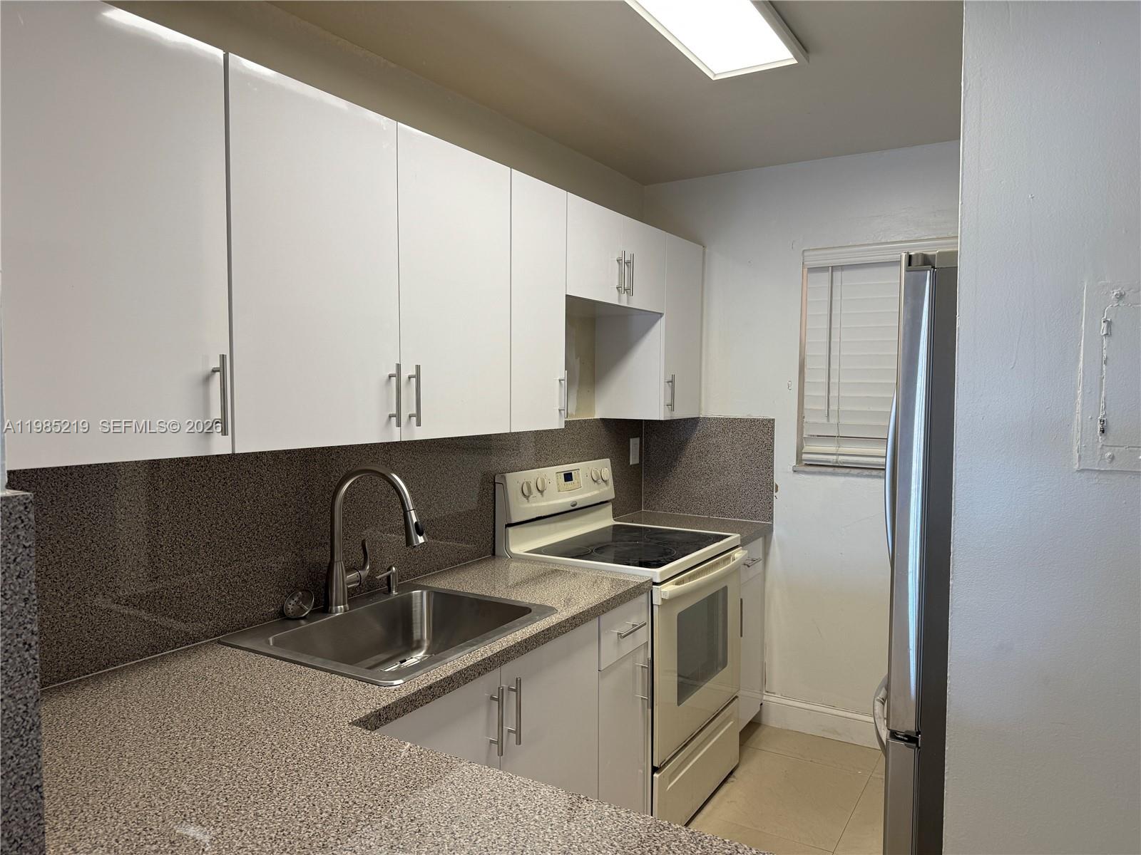 A kitchen features white cabinets, speckled countertops, a stainless steel sink, and white appliances — 6055 W 19th Ave # 311, Hialeah FL 33012, HIALEAH, FL