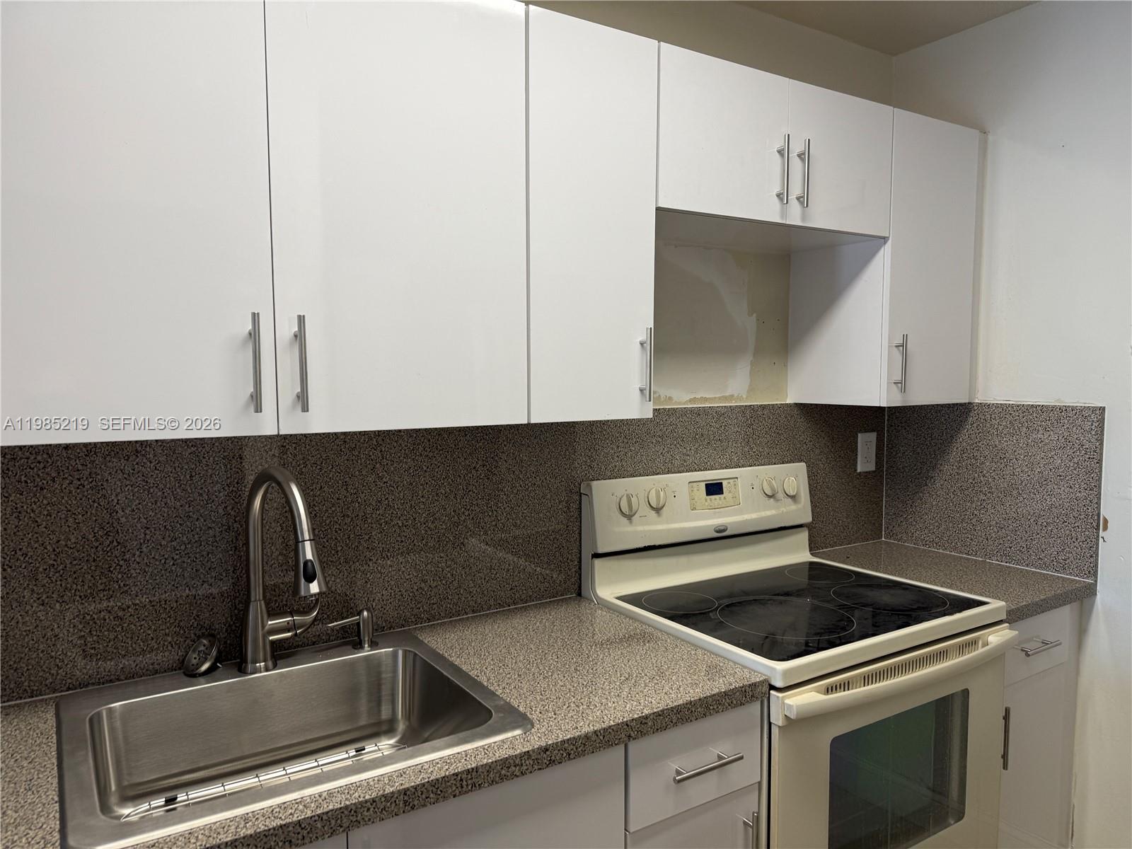 A kitchen features white cabinets, a speckled countertop, a stainless steel sink, and an oven — 6055 W 19th Ave # 311, Hialeah FL 33012, HIALEAH, FL