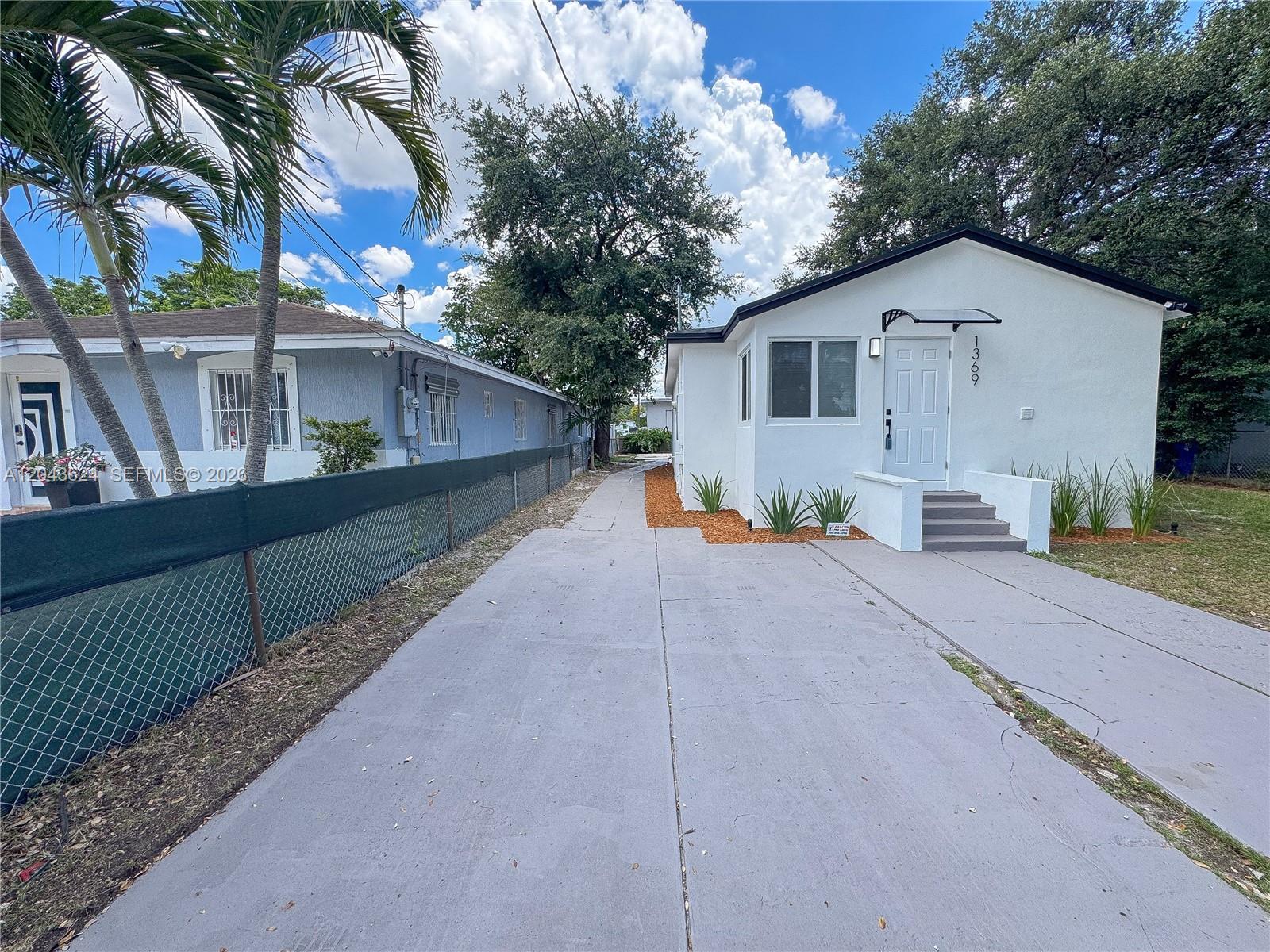 A white house with a driveway and a chain-link fence sits under a blue sky — 1369 NW 68th Ter, Miami FL 33147, MIAMI, FL