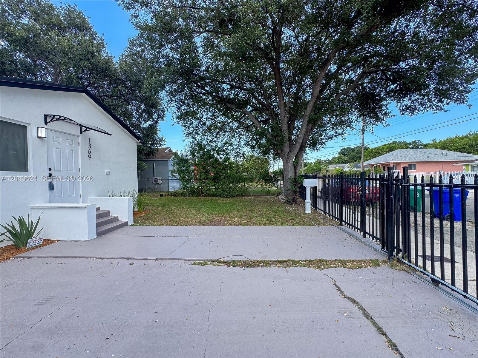 A white house with a concrete driveway and a black metal fence in the front yard — 1369 NW 68th Ter, Miami FL 33147, MIAMI, FL