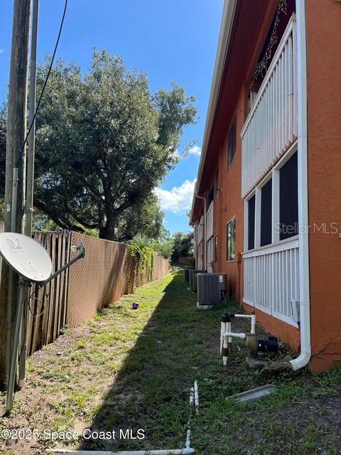 A narrow grassy side yard runs between a chain-link fence and an orange building — 2755 BARNA AVENUE, TITUSVILLE, FL