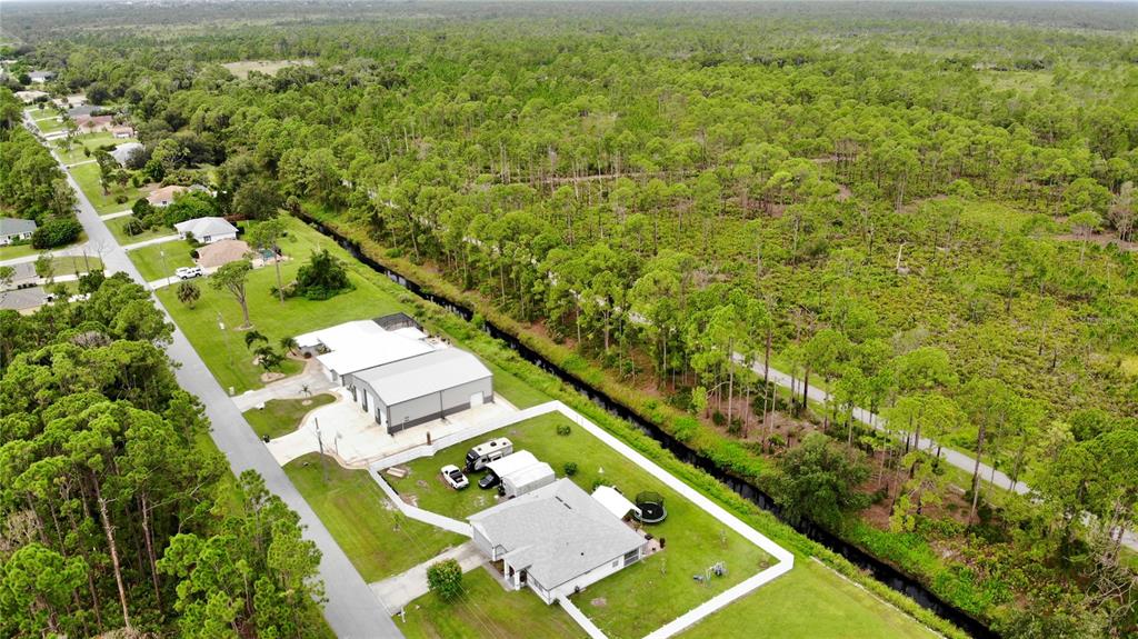 An aerial view shows a residential street with houses, a large metal workshop, and a canal — TALLY HO ROAD, NORTH PORT, FL