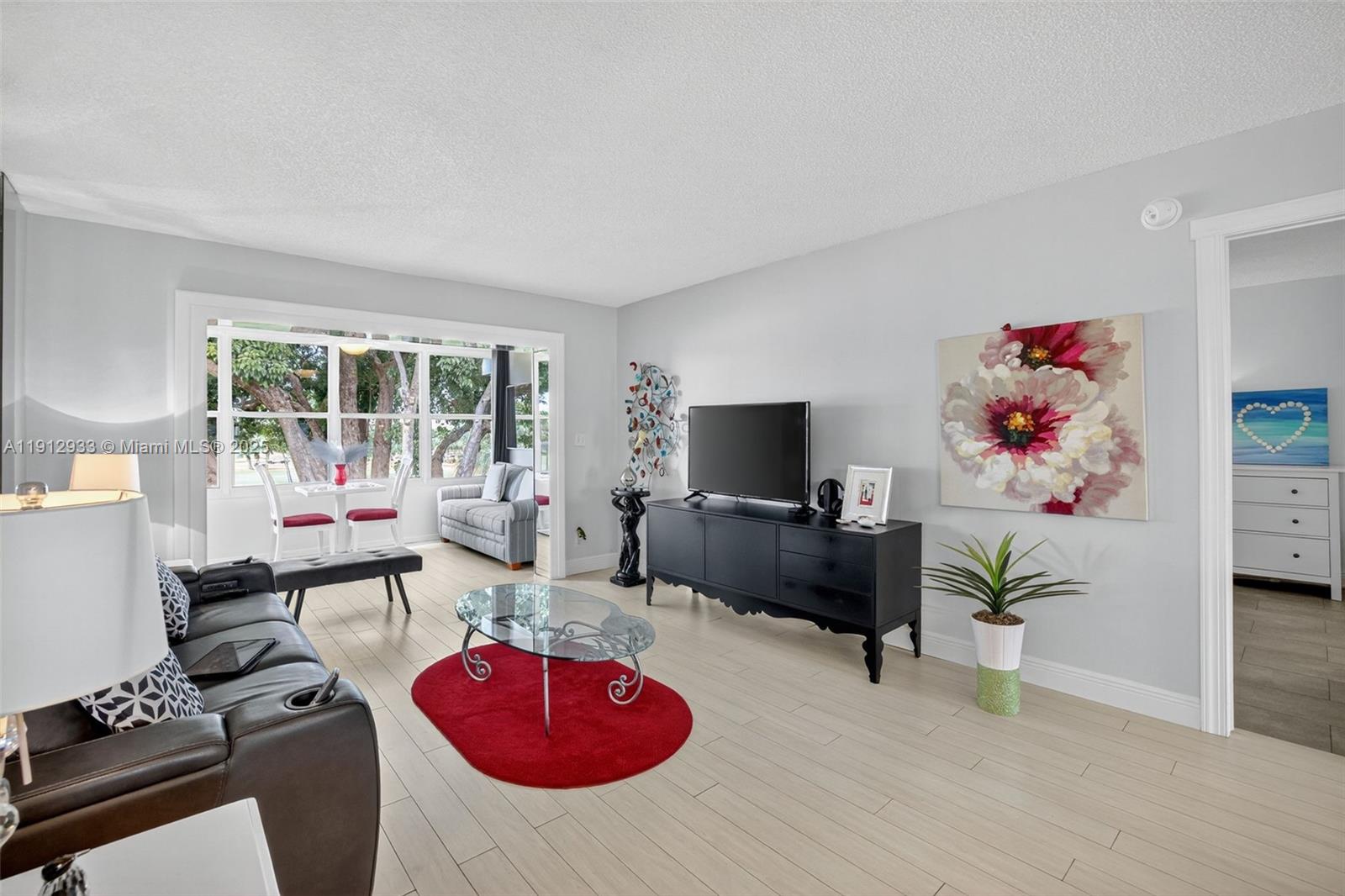 A living room features light wood-look flooring, a black media console, and a red rug — 7817 Golf Circle Dr # 305, Margate FL 33063, MARGATE, FL