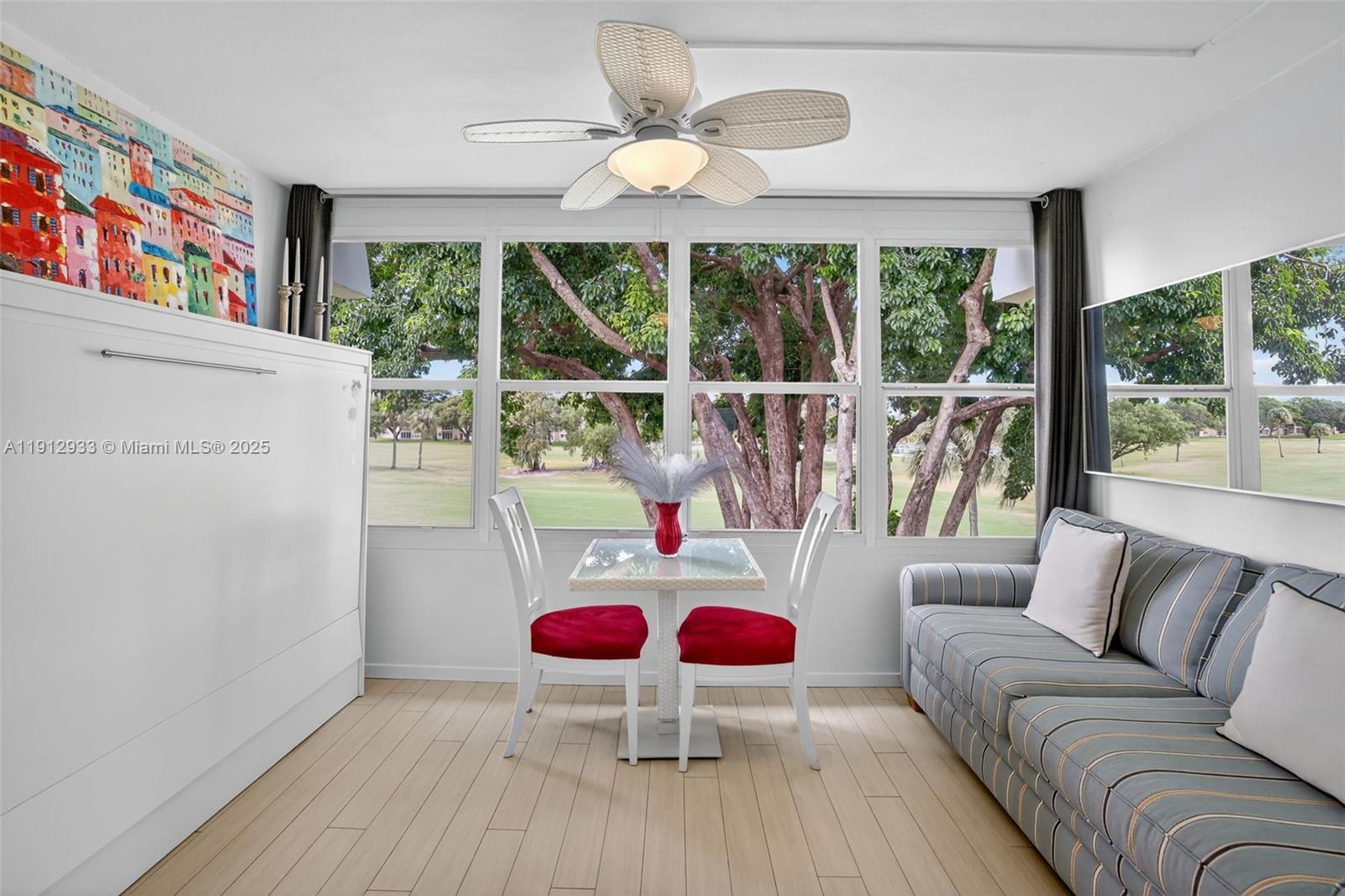 A room with a striped sofa, a small dining set, and large windows overlooking trees — 7817 Golf Circle Dr # 305, Margate FL 33063, MARGATE, FL
