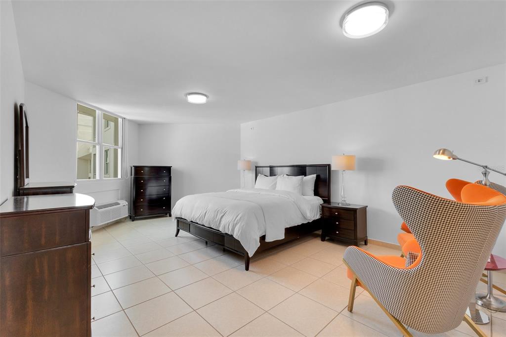 A bedroom features a dark wood bed frame, matching furniture, tiled floors, and orange accent chairs — 100 CALLE DEL MUELLE UNIT 21007, OLD SAN JUAN, PR