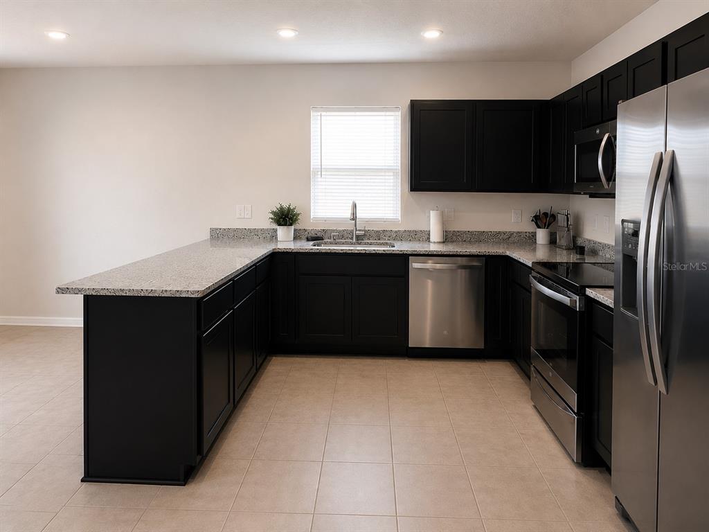 A kitchen features black cabinets, granite countertops, stainless steel appliances, and light tile flooring — 614 MANCHESTER PATH, DUNDEE, FL