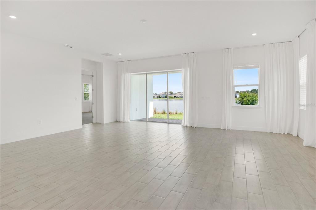 A bright, empty living room features light-colored tile flooring, white walls, and large sliding glass doors — 13589 MCMILLAN DRIVE, ORLANDO, FL