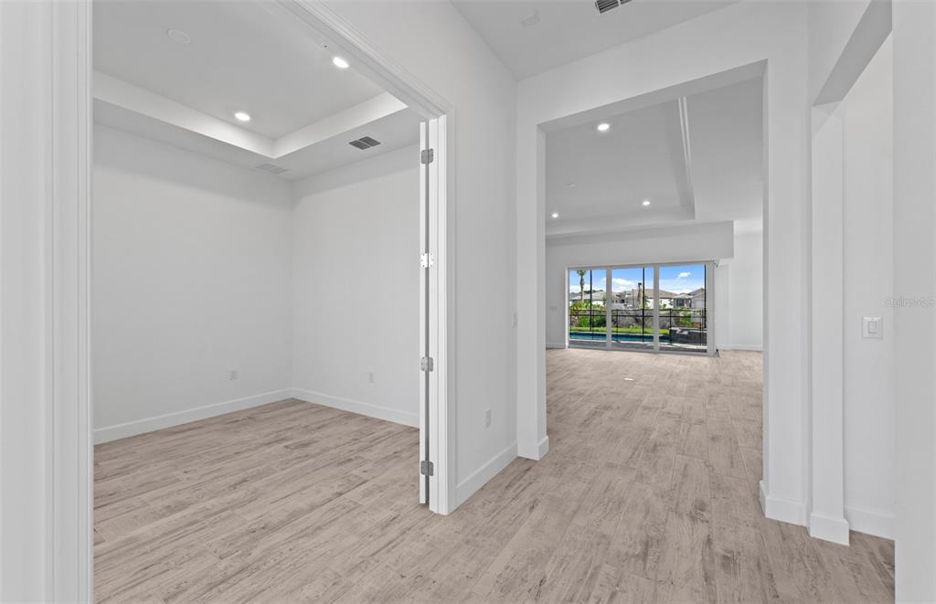 A bright room with wood-look tile flooring leads to an open living area with sliding doors — 26537 SANDY HILL CIRCLE, ENGLEWOOD, FL