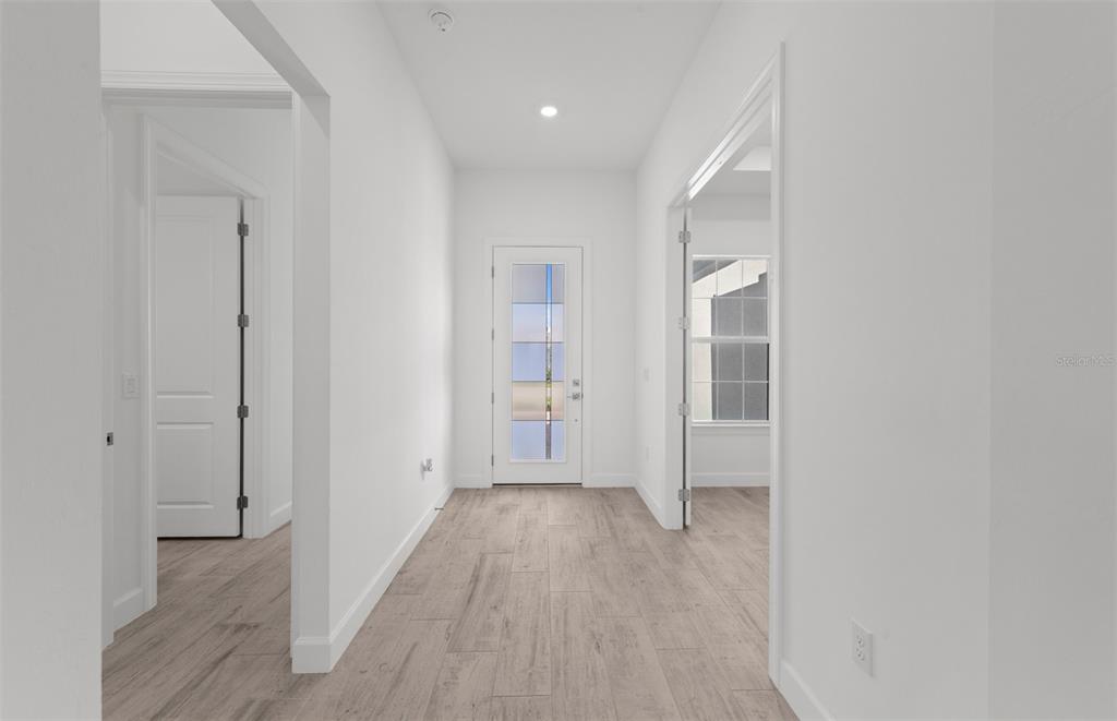 A bright hallway with light wood-look flooring leads to a glass-paneled front door — 26537 SANDY HILL CIRCLE, ENGLEWOOD, FL