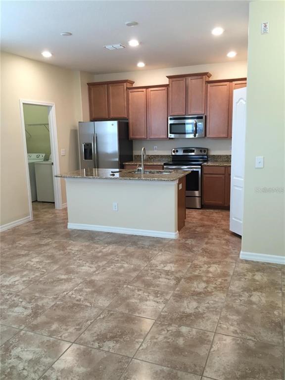 A kitchen features wood cabinets, stainless steel appliances, a granite island, and tiled flooring — 5618 WATER ROSE ROAD, WINTER GARDEN, FL