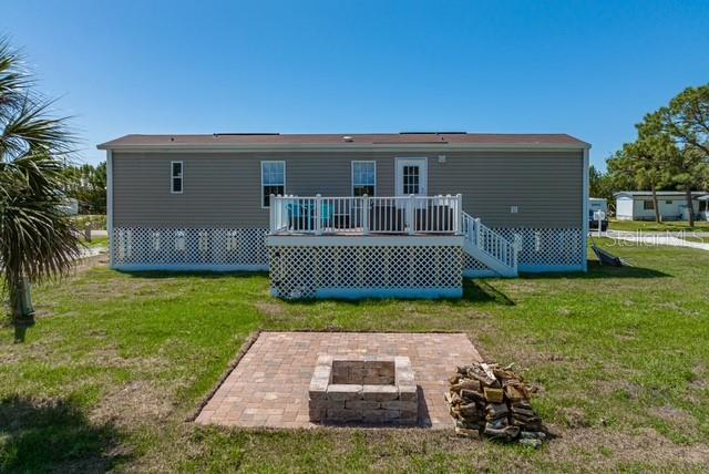 The exterior of a manufactured home features a raised deck and a stone fire pit — 14428 STEPHENS ROAD, PORT CHARLOTTE, FL