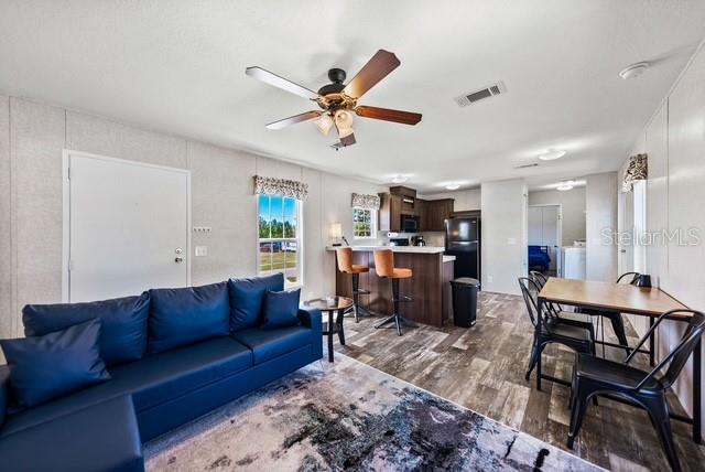 A living room with a blue sofa, ceiling fan, and an open kitchen with bar seating — 14428 STEPHENS ROAD, PORT CHARLOTTE, FL