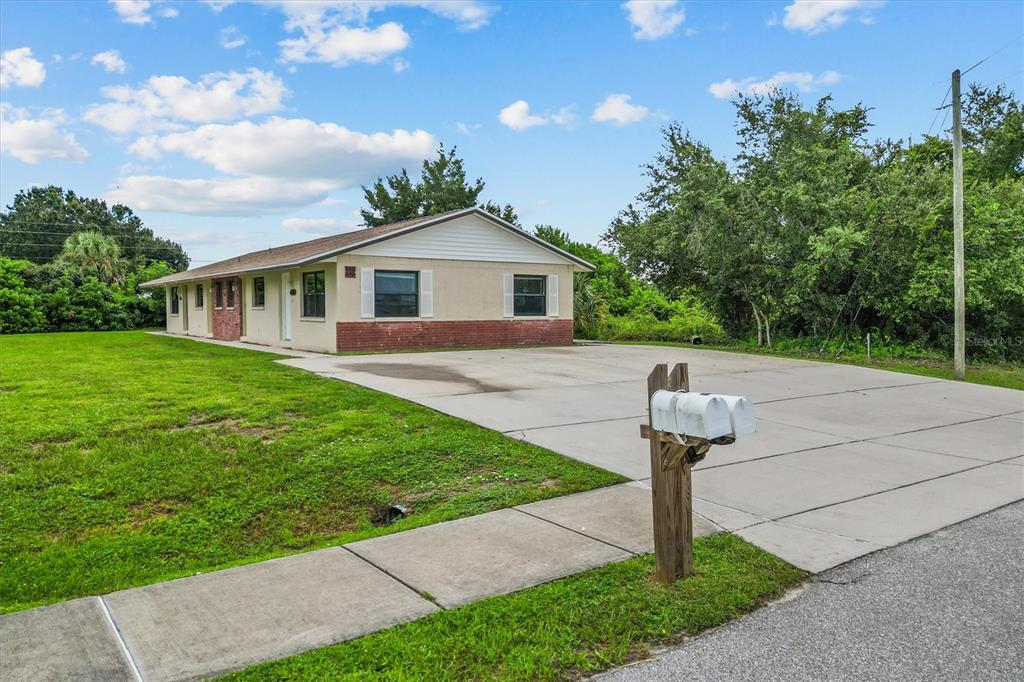 A single-story duplex with a large concrete driveway and two mailboxes sits on a lawn — 27242 SUNNYBROOK ROAD, PUNTA GORDA, FL