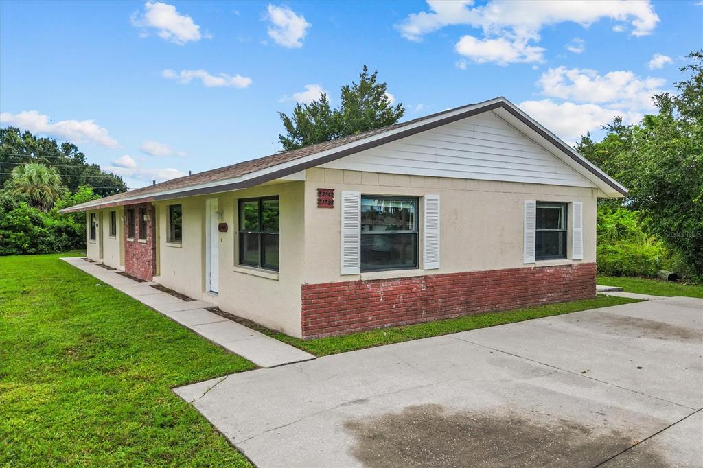 A single-story duplex with a tan stucco exterior, red brick accents, and a concrete driveway — 27242 SUNNYBROOK ROAD, PUNTA GORDA, FL