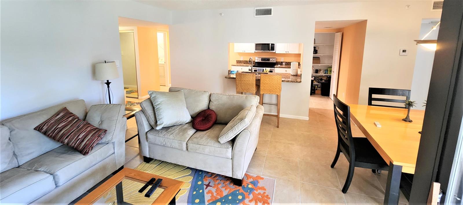 A living room with a sofa, dining area, and kitchen pass-through with bar stools — 1915 Lavers Circle # E208, Delray Beach FL 33444, DELRAY BEACH, FL