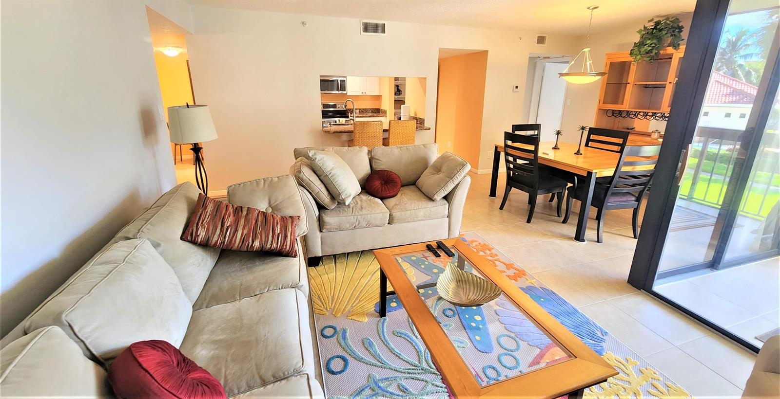 A living room with a beige sofa, loveseat, coffee table, and dining area near a balcony — 1915 Lavers Circle # E208, Delray Beach FL 33444, DELRAY BEACH, FL