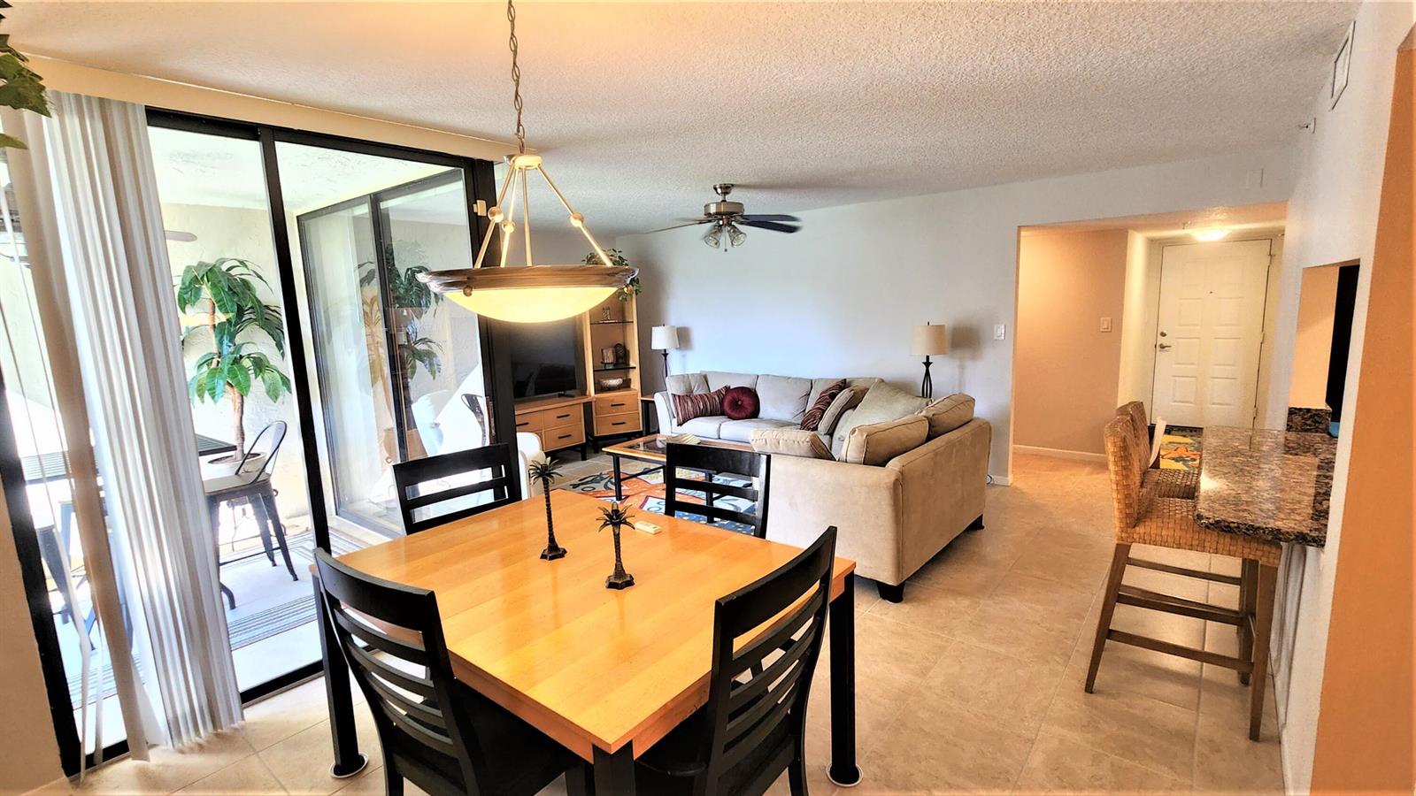 A dining area with a wooden table leads into a living room with a sofa — 1915 Lavers Circle # E208, Delray Beach FL 33444, DELRAY BEACH, FL