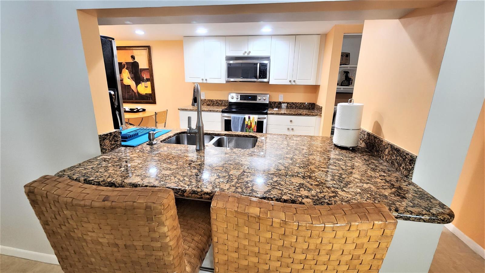 A kitchen features white cabinets, granite countertops, a stainless steel stove, and a breakfast bar — 1915 Lavers Circle # E208, Delray Beach FL 33444, DELRAY BEACH, FL