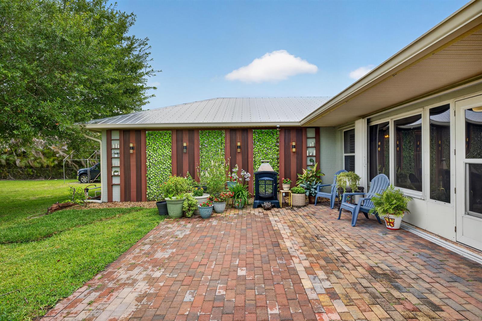 A brick patio sits beside a house exterior featuring vertical wood panels and green foliage — 5606 Silver Oak Drive, Fort Pierce FL 34982, FORT PIERCE, FL